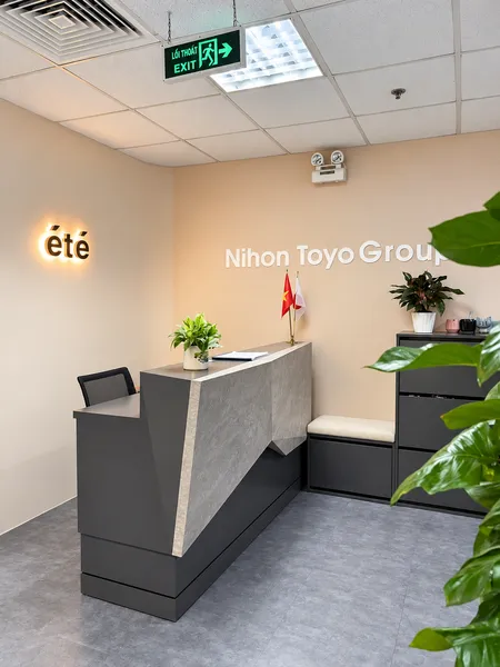 Khu vực lễ tân văn phòng ÉTé thiết kế hiện đại, sang trọng với quầy lễ tân màu xám đá, logo đèn sáng và cây xanh trang trí